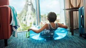 A child sitting on a blue inflatable pool in a hotel room with a large window, a red armchair, and a suitcase. - Universal's Cabana Bay Beach Resort (Orlando)