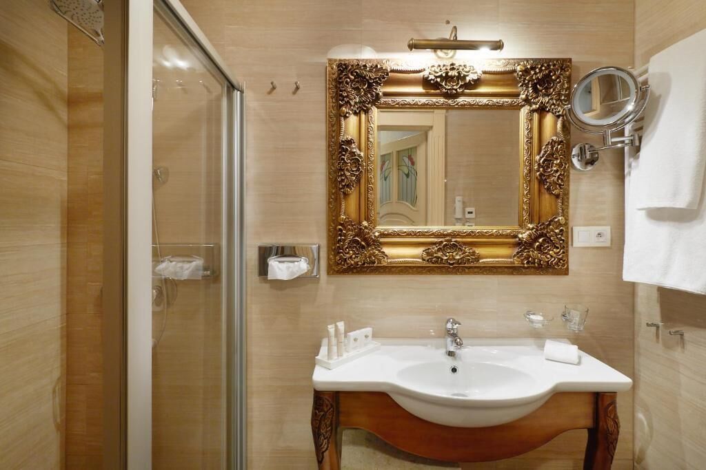 A bathroom with a large ornate mirror, a sink, and a glass shower enclosure.