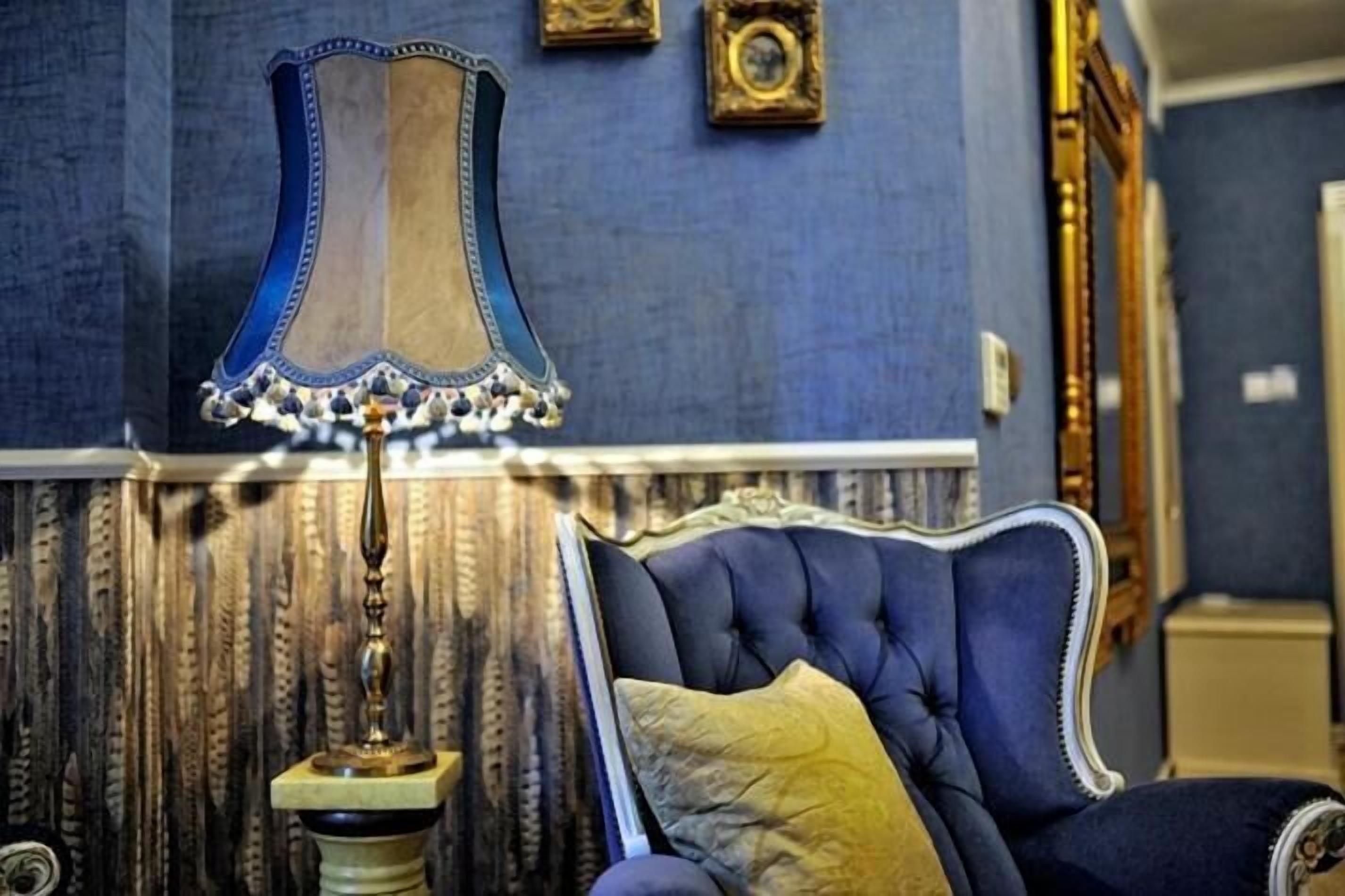 Ein Zimmer mit einem blau gepolsterten Sessel, einer dekorativen Lampe und einer Wand mit Muster.