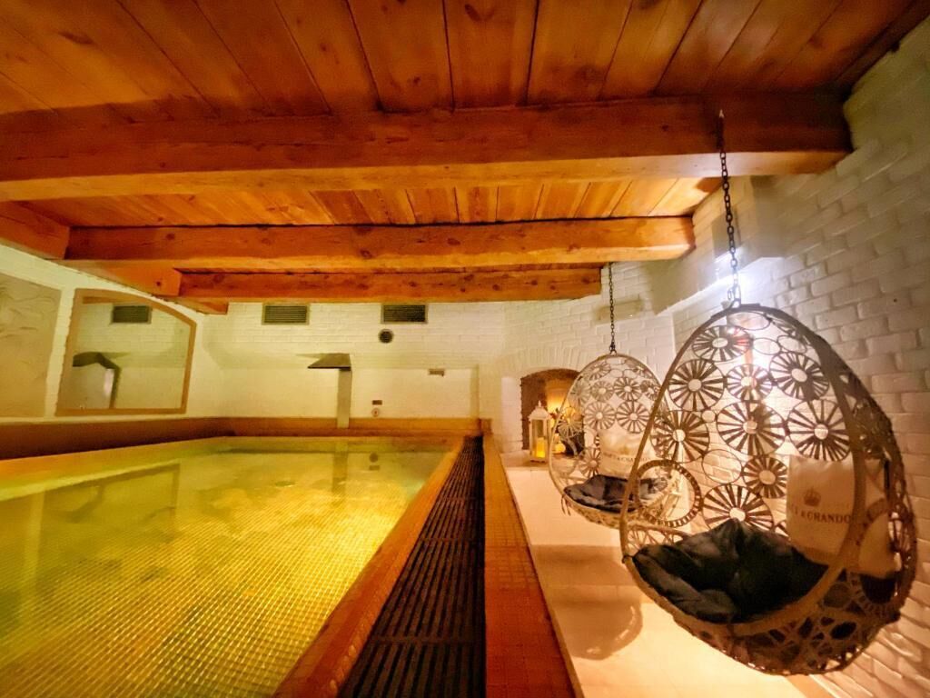 A spa room with a wooden ceiling, a hot tub, and hanging chairs.