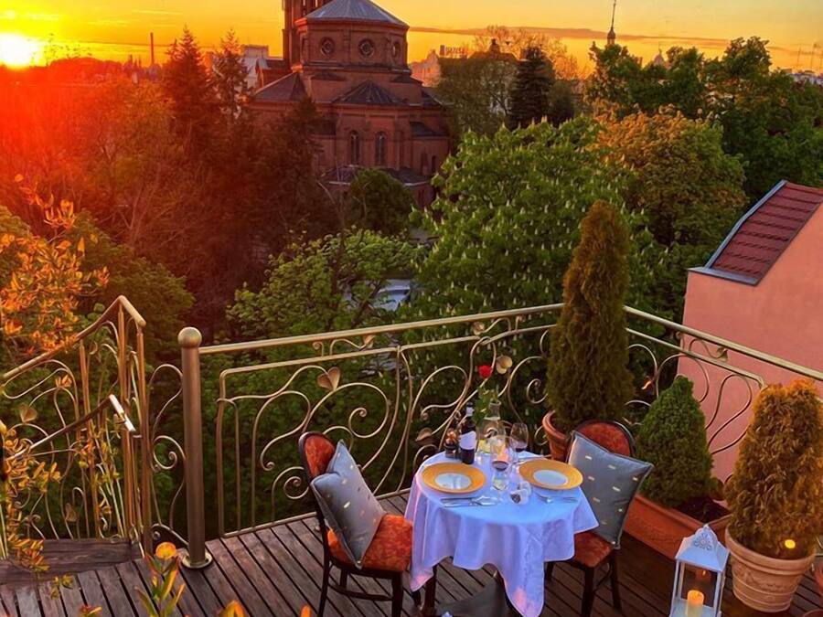 Una terraza con una mesa preparada para dos, con vista a una iglesia y al atardecer.