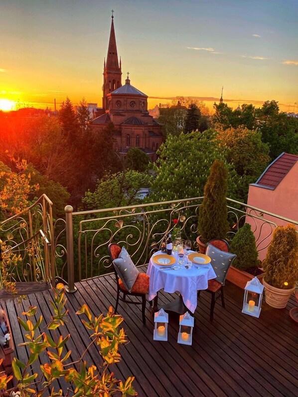 A deck with a table set for two, overlooking a church and a sunset. - Hotel Bohema (Bydgoszcz)