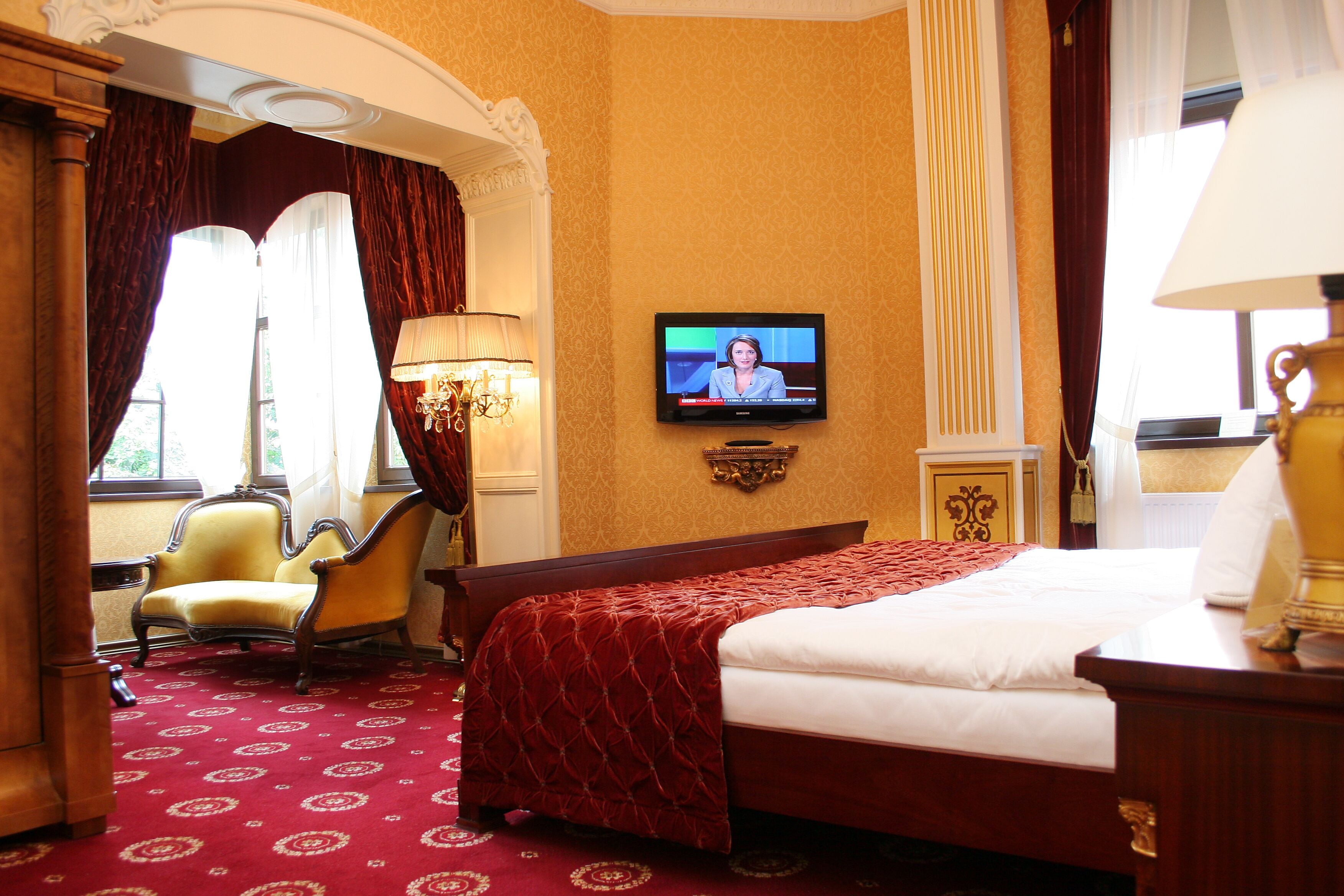 A hotel room with a large bed, a television mounted on the wall, a chair, and a lamp.