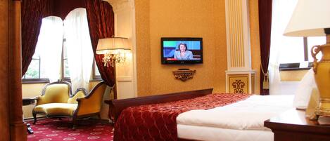 A hotel room with a large bed, a television mounted on the wall, a chair, and a lamp.
