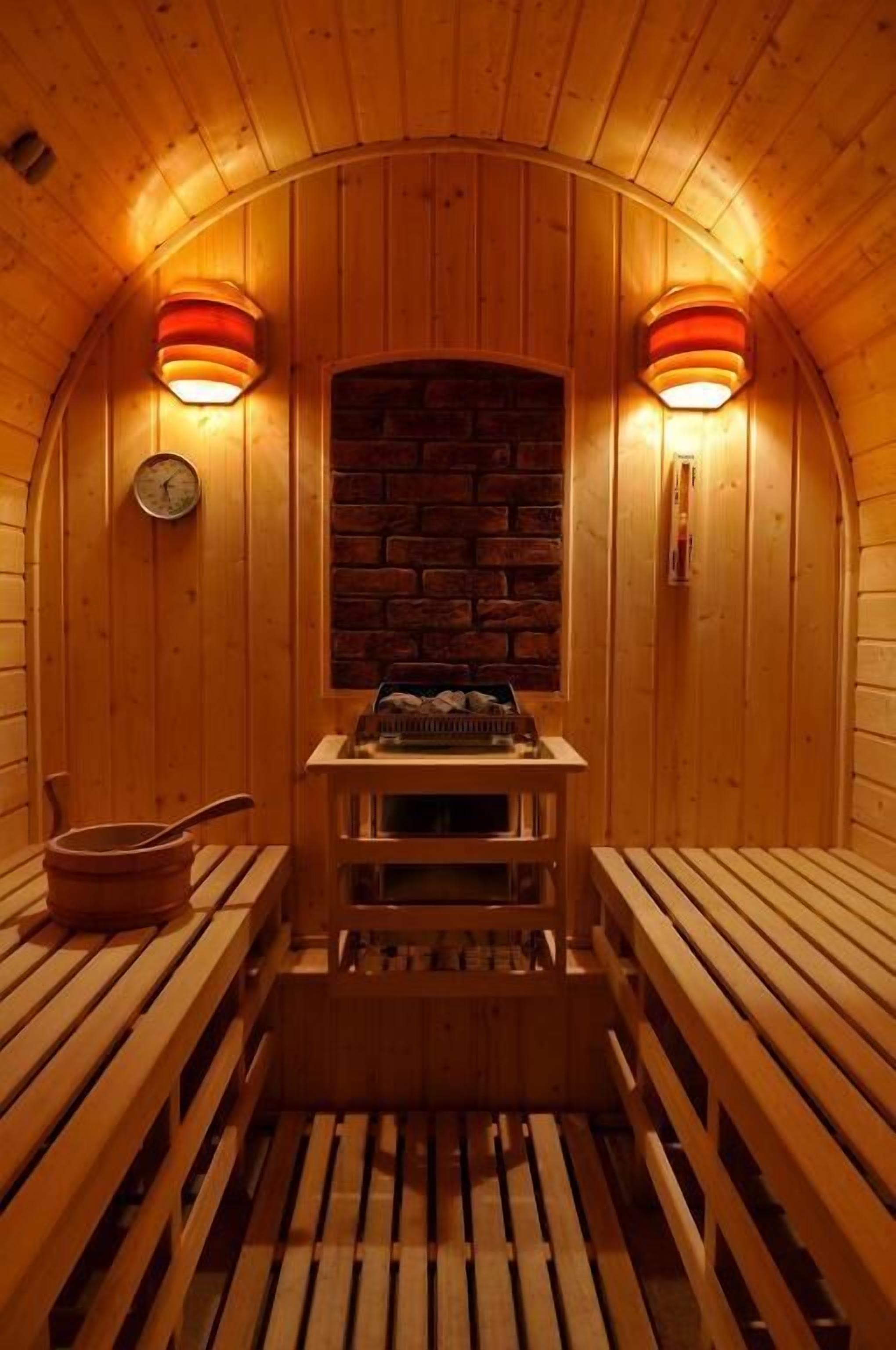 Una sauna con bancos de madera, un muro de ladrillo y dos lámparas fijadas a la pared.
