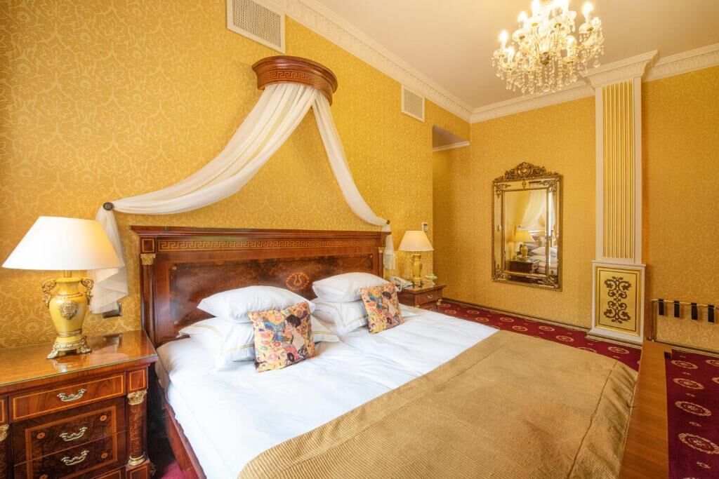 Una habitación de hotel con una cama con dosel, una araña, un espejo grande y una alfombra roja.