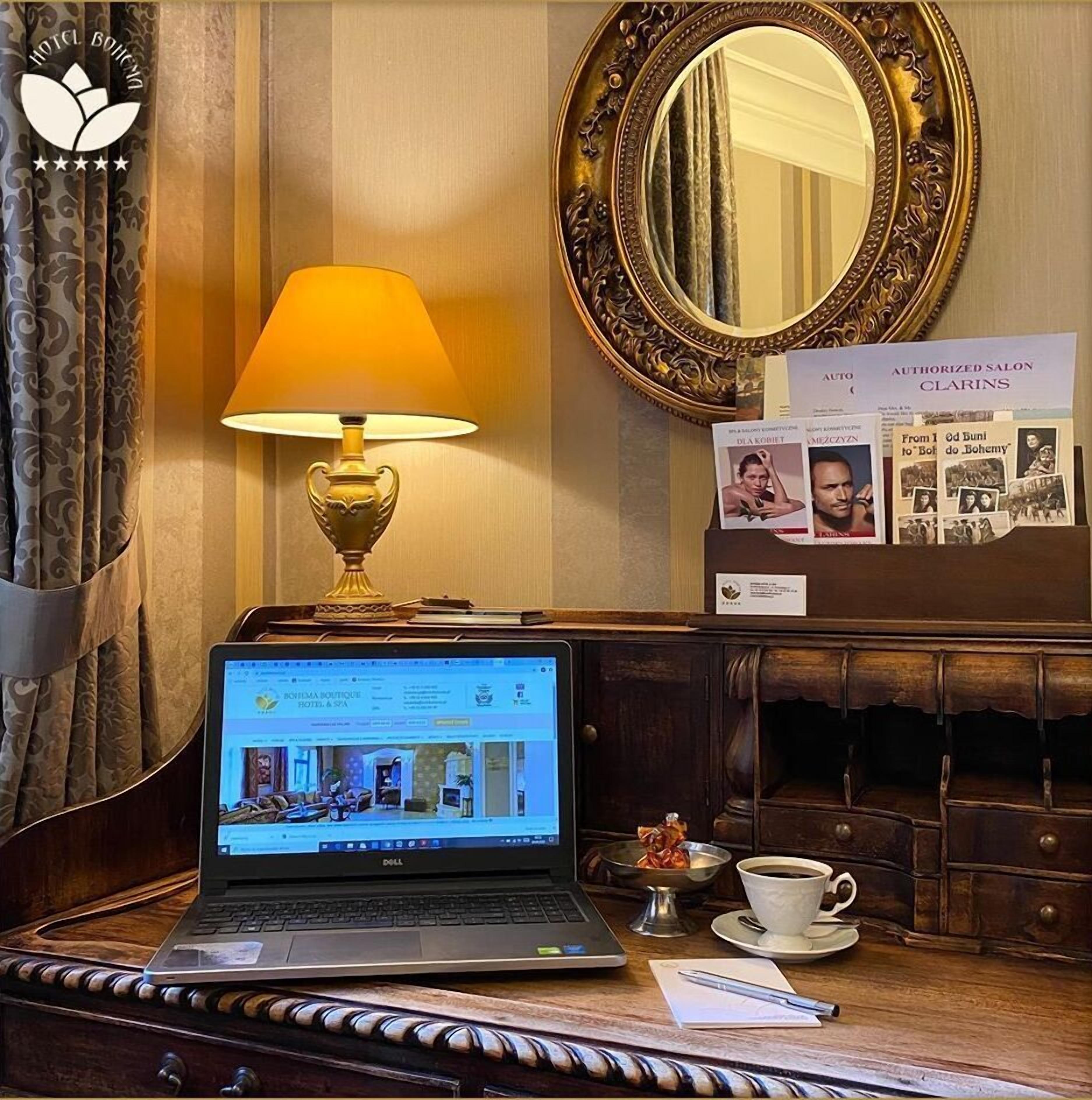 A laptop on a wooden desk with a lamp, a cup of coffee, and a framed mirror.