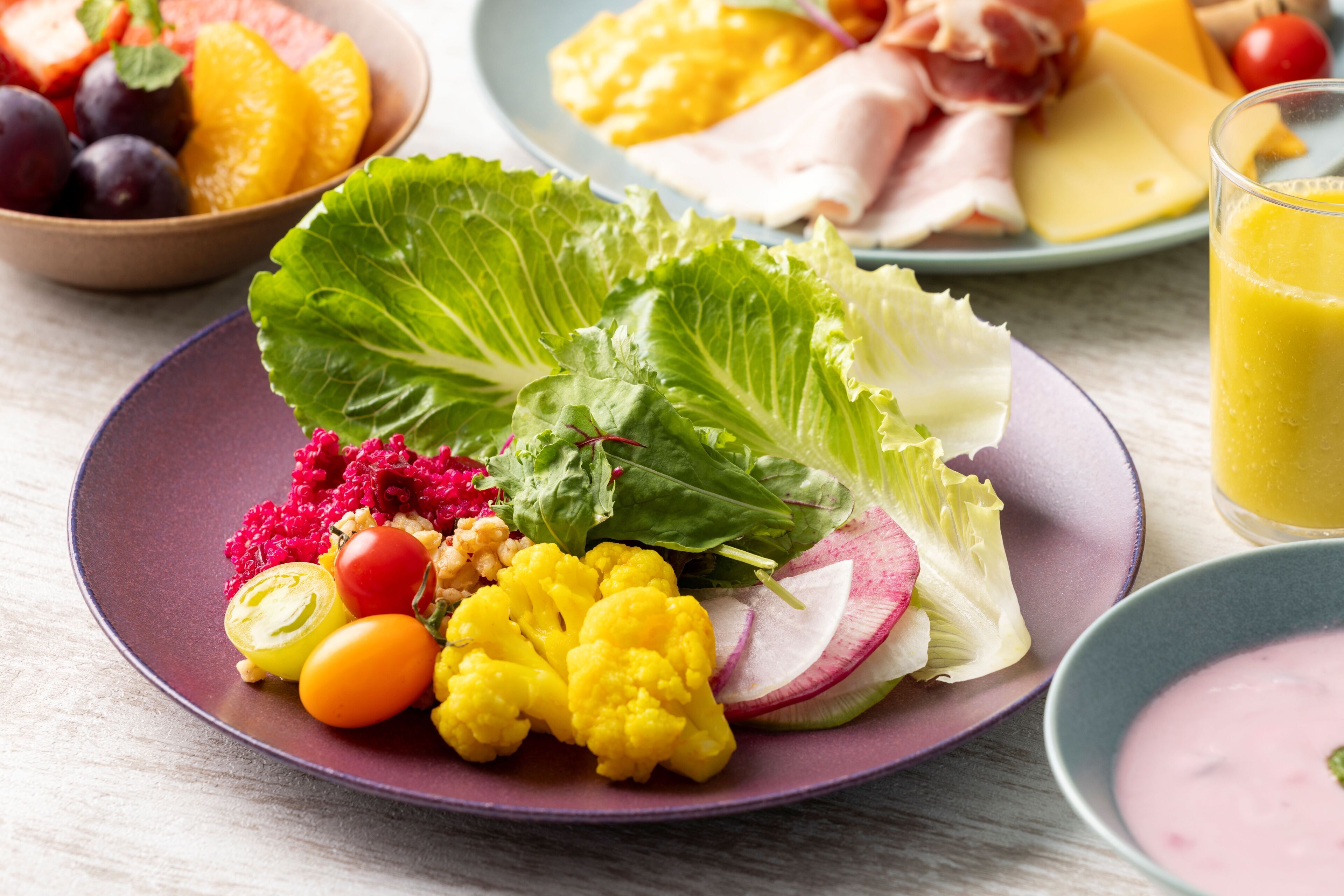 Une assiette remplie de légumes et de fruits frais, notamment de la laitue, des radis, des tomates et du chou-fleur, le tout présenté sur une assiette violette.