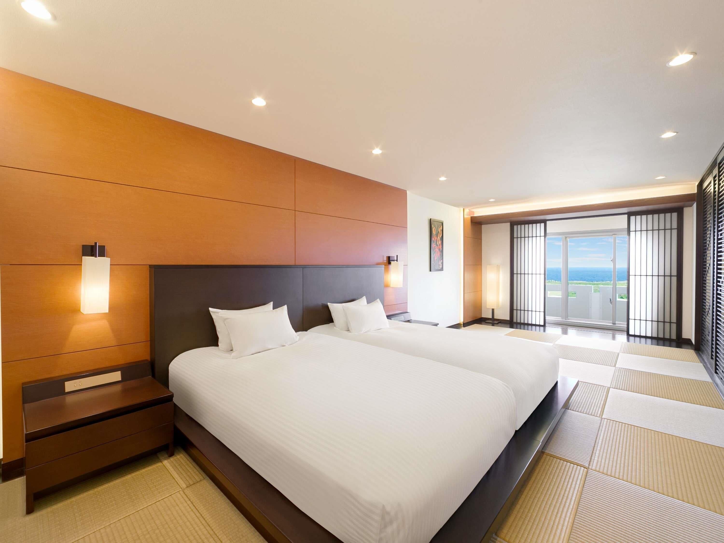 A hotel room with two beds, a large window, and a view of the sea.