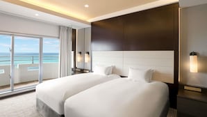 Habitación de hotel con dos camas, un ventanal con vista al océano y un balcón.