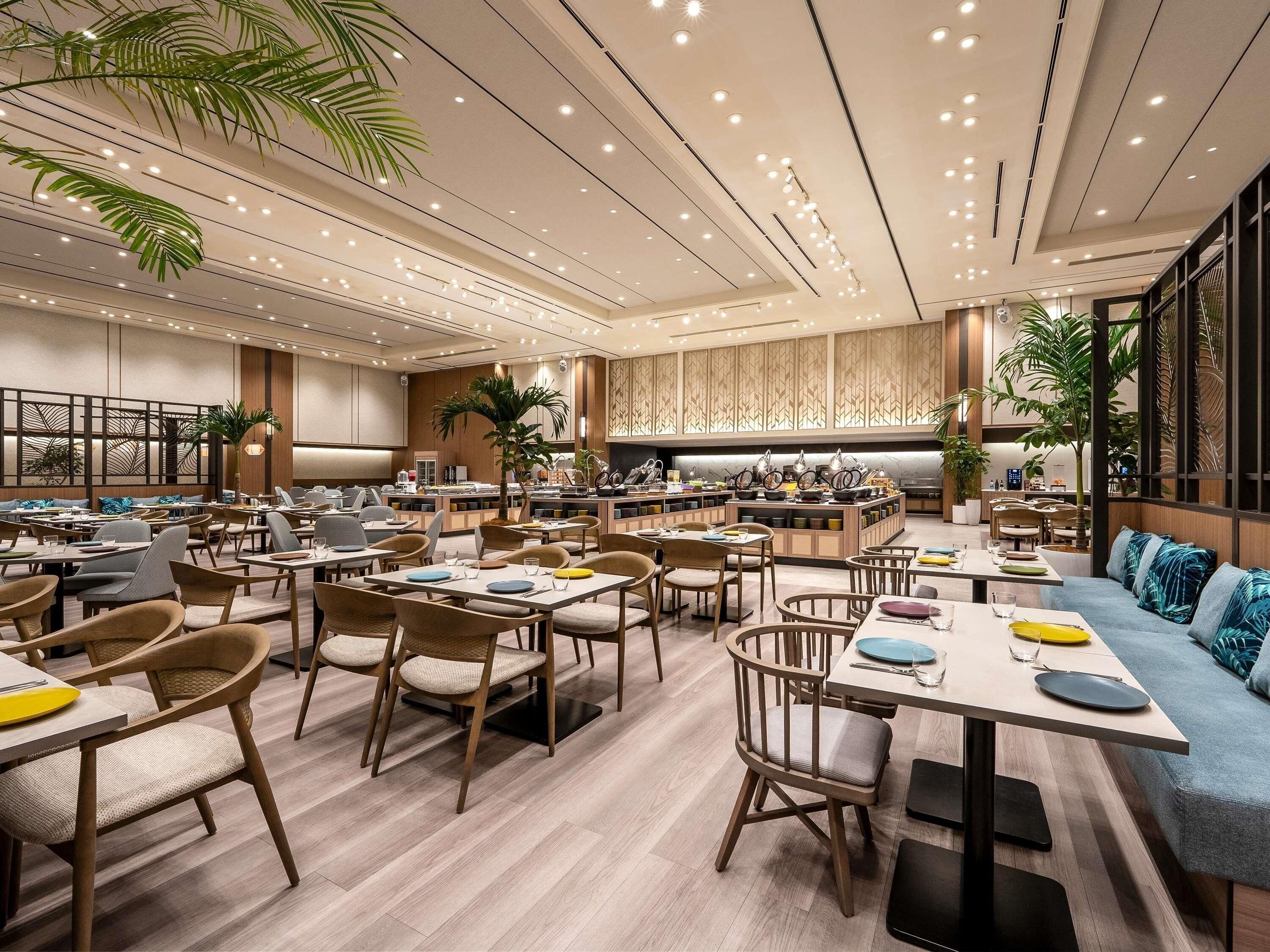 A spacious restaurant with multiple dining areas, wooden furniture, and a modern ceiling design.