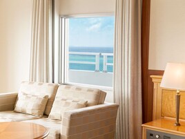 Habitación de hotel con sofá, una mesa redonda, una lámpara y vista al océano a través de una ventana.