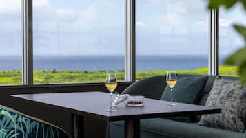 Una stanza con vista sull'oceano, un tavolo con due bicchieri di vino e un divano verde con un cuscino.