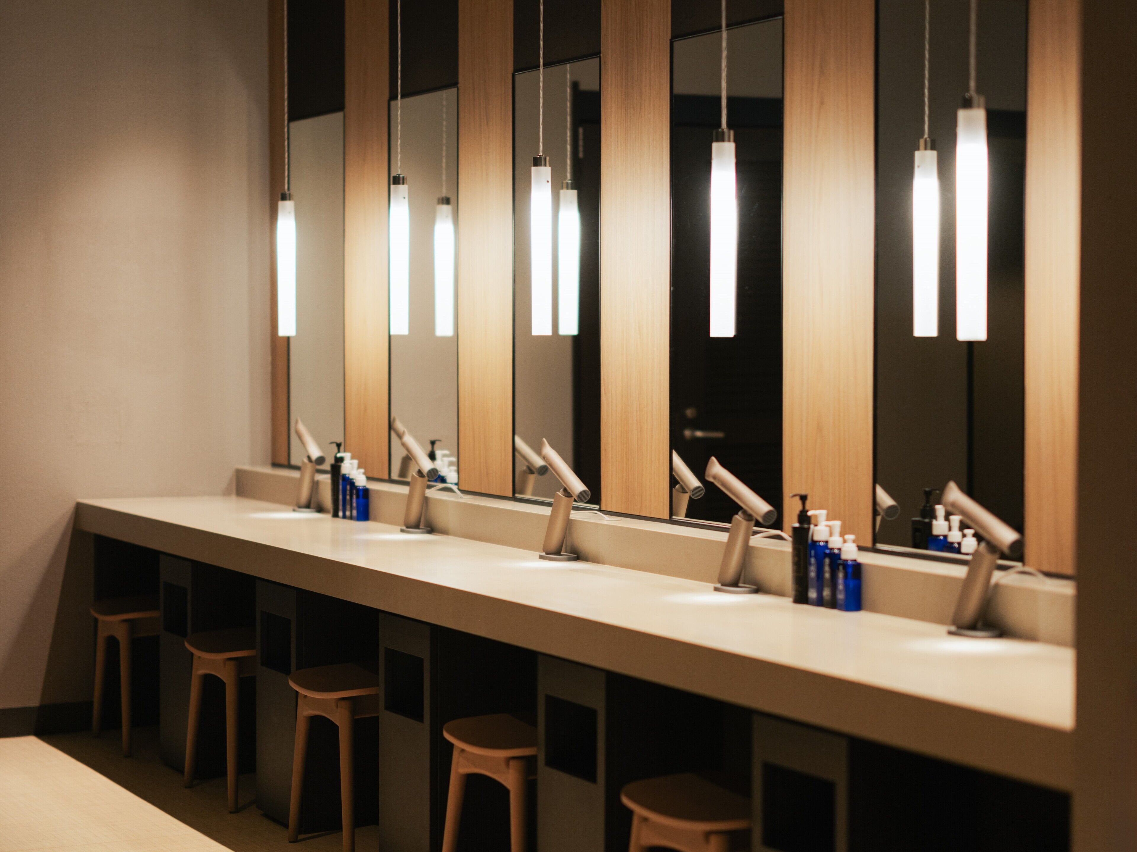 A modern bathroom with multiple sinks, mirrors, and stools.