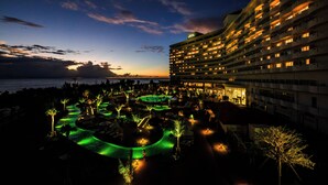 Un hotel de varios pisos, con zona de piscina y vista al océano al atardecer.