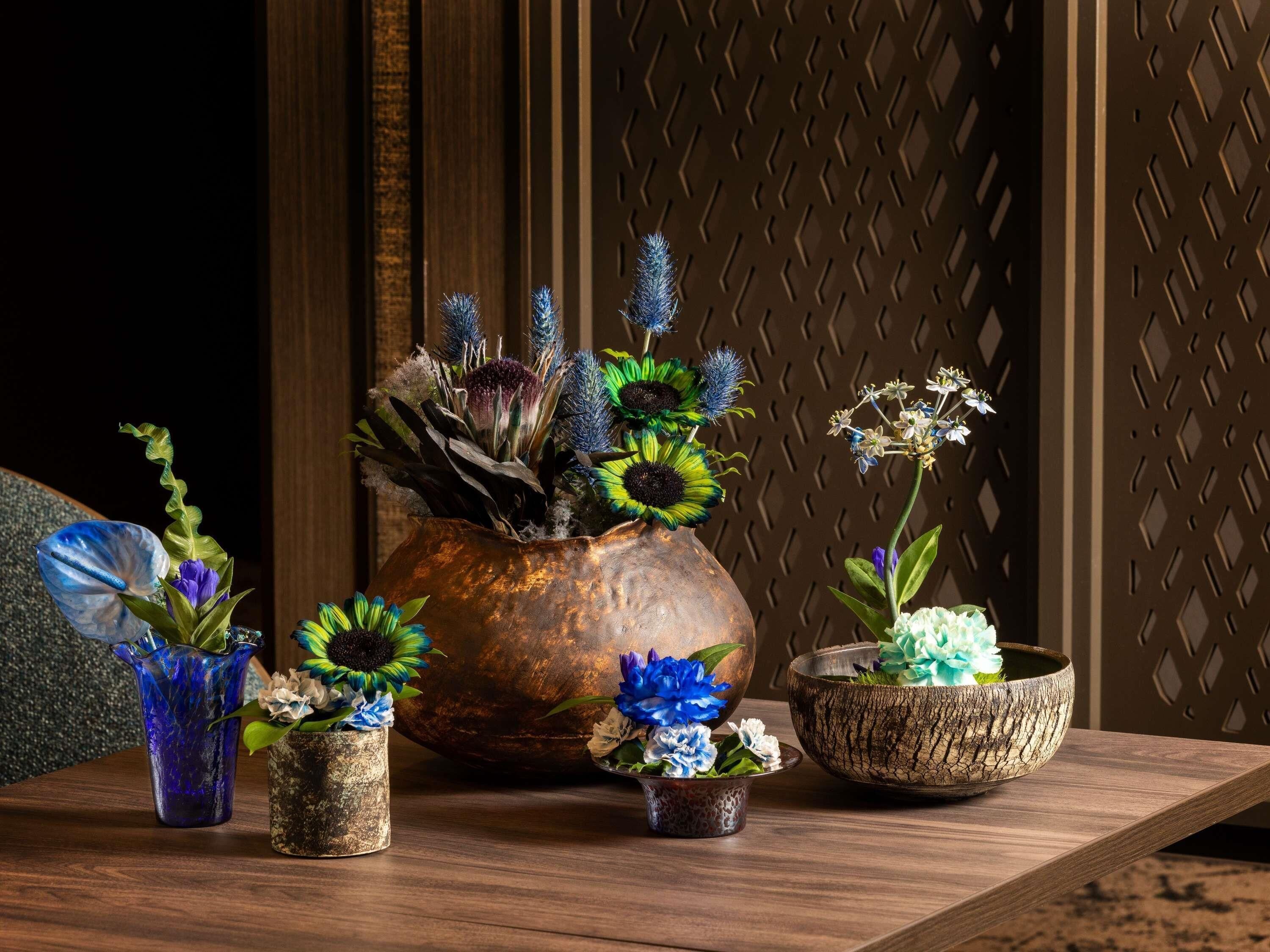 A wooden table with various flower arrangements in different containers.