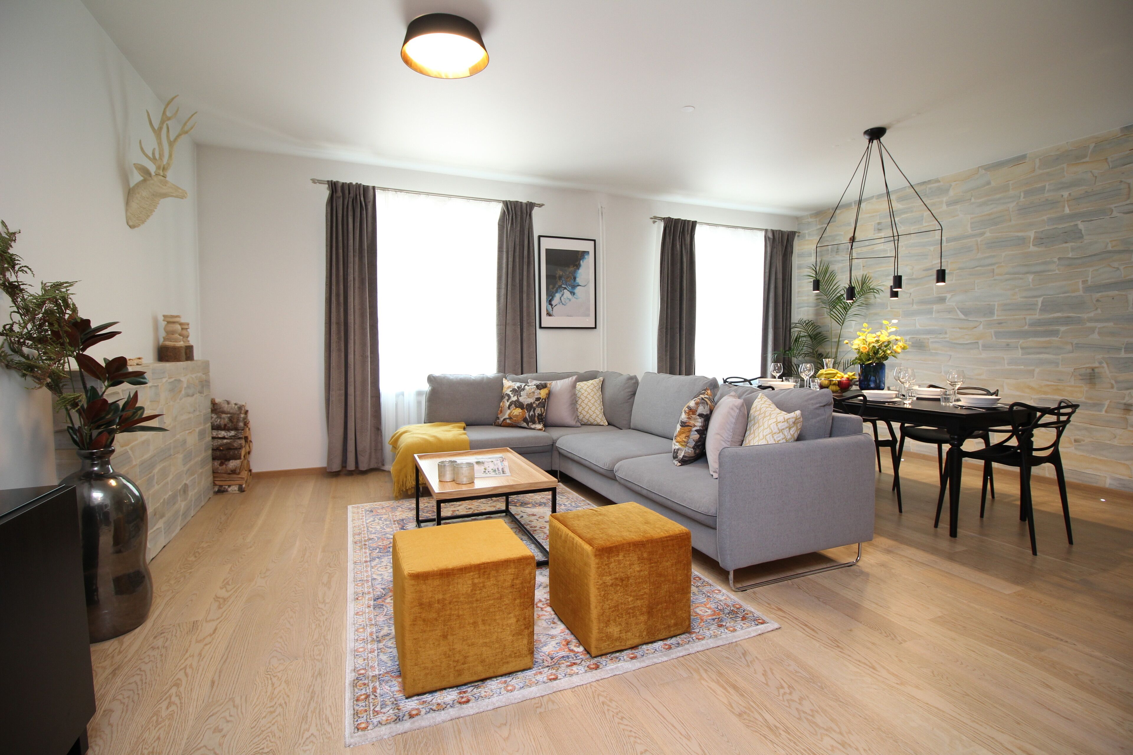 Un salon moderne avec un canapé gris, deux poufs, une table basse et un coin repas comprenant une table et des chaises.