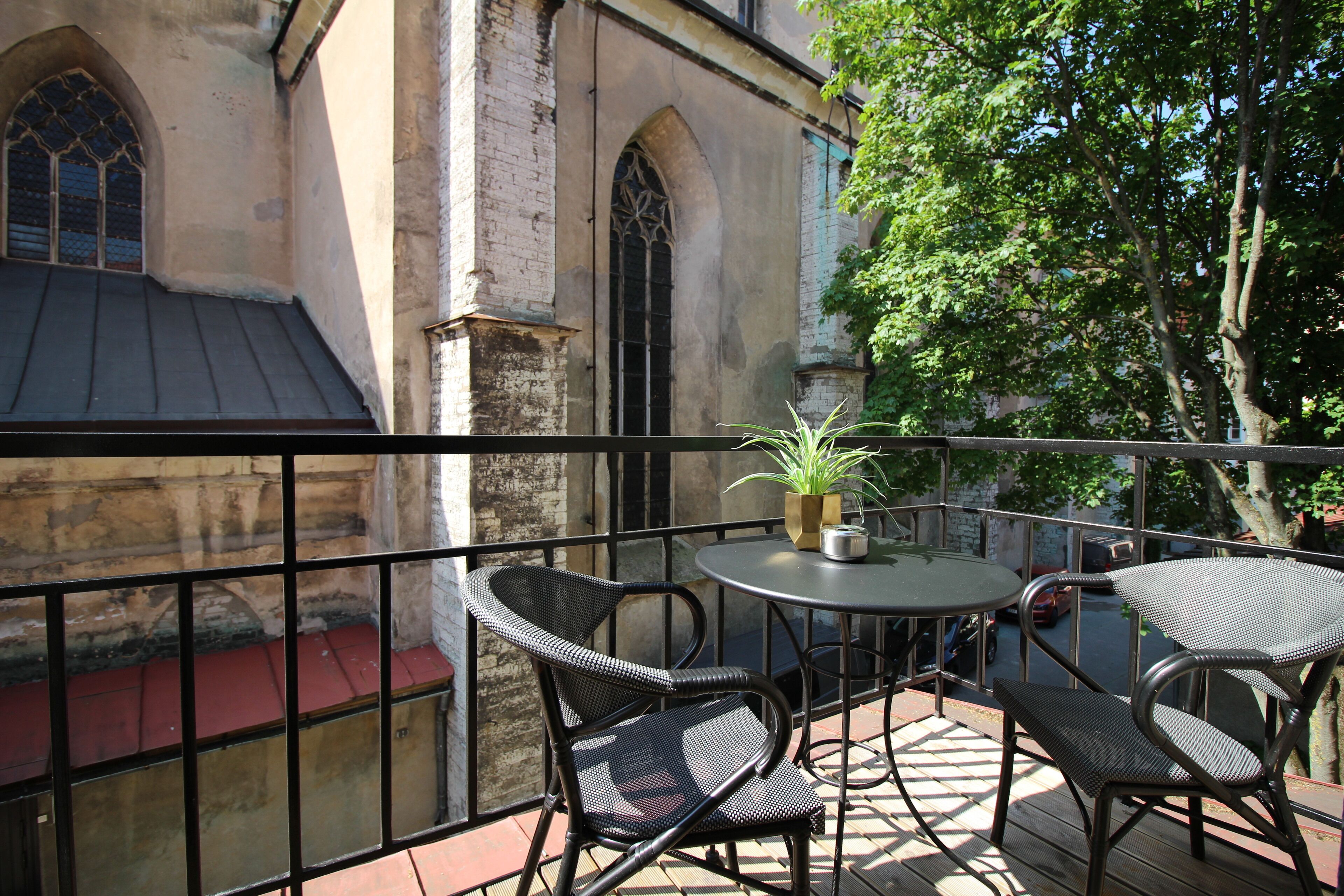 A balcony with wicker chairs and a table, overlooking a historic building with arched windows.