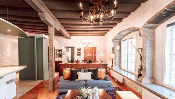 Un vaste espace de vie doté d’un plafond en bois, d’un canapé bleu agrémenté de coussins décoratifs, d’une table basse en bois et d’une grande fenêtre laissant entrer la lumière naturelle.