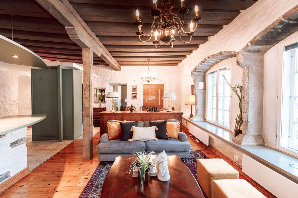 Un vaste espace de vie doté d’un plafond en bois, d’un canapé bleu agrémenté de coussins décoratifs, d’une table basse en bois et d’une grande fenêtre laissant entrer la lumière naturelle.