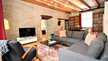 Una sala de estar acogedora con un sofá gris, una mesa de centro negra, un televisor de pantalla plana y una estantería.