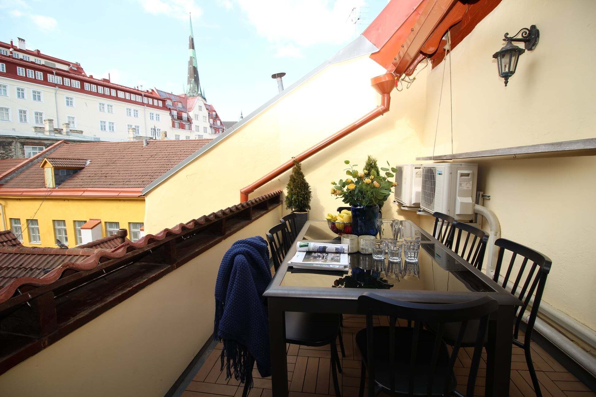 A balcony with a table, chairs, a potted plant, and air conditioning units.