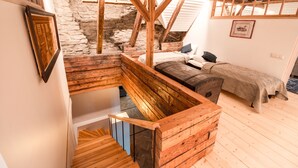 Une chambre mansardée au style rustique, avec des poutres apparentes, un mur en pierre et un lit en mezzanine.