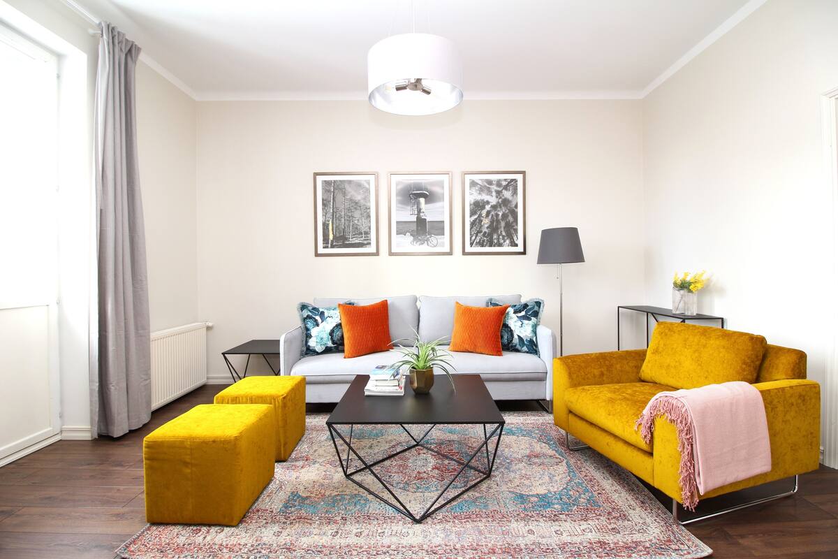 Un salon comprenant un canapé, des poufs, une table basse et une lampe.
