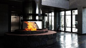 Una chimenea moderna en el interior con detalles de piedra, ventanas amplias y un techo alto.
