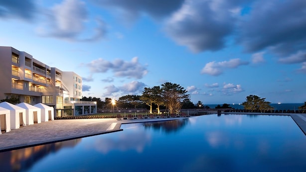 Un hotel moderno con piscina, mobiliario exterior y vista al mar.