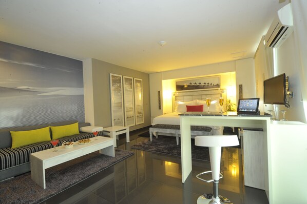 A modern hotel room with a large bed, a desk with a computer, a sofa with cushions, and a painting on the wall. - Le Trianon Luxury Hotel & Spa (Casablanca)