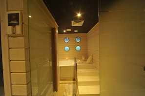 A modern bathroom with a glass shower enclosure, a bathtub, and a small seating area with a towel. - Le Trianon Luxury Hotel & Spa (Casablanca)