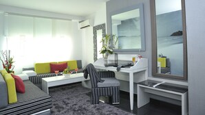 Ein modernes Wohnzimmer mit einer Couch, einem Sessel und einem Couchtisch. An der Wand befindet sich ein großer Spiegel und ein Fenster sorgt für natürliches Licht.