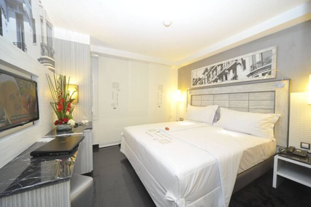 A hotel room with a bed, bedside table, lamp, and a desk with a laptop.