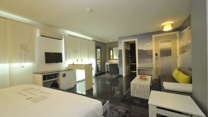 Ein modernes Hotelzimmer mit einem Bett, einem kleinen Schreibtisch, einer Couch, einem Fernseher und einer Küchenzeile.