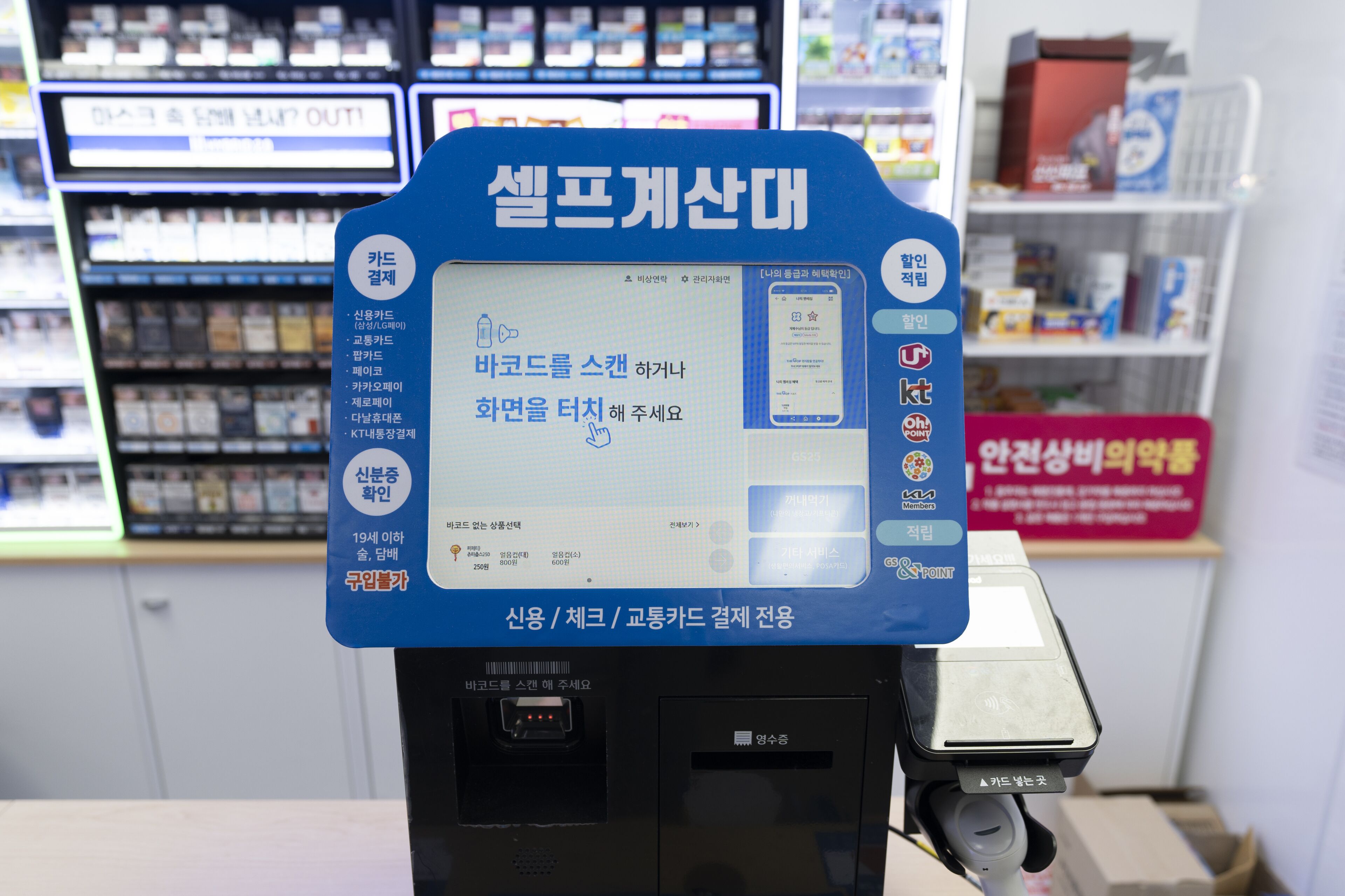 Un quiosco autoservicio con un letrero azul, una pantalla informativa y un lector de códigos de barras.