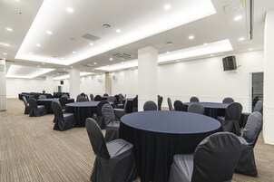 Un salón de conferencias con mesas y sillas redondas, paredes blancas e iluminación en el techo.
