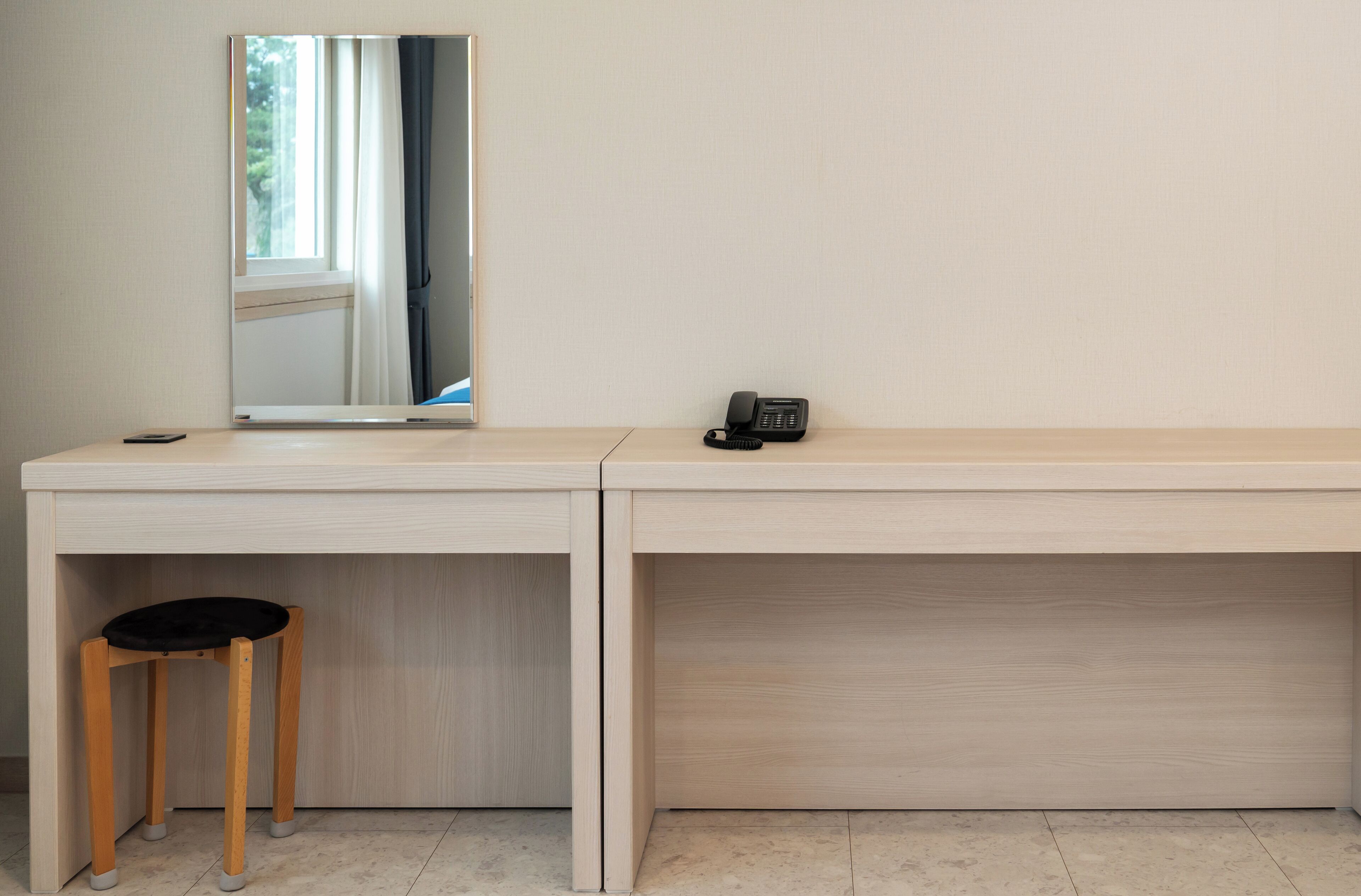 A modern desk with a mirror, a telephone, and a small stool.