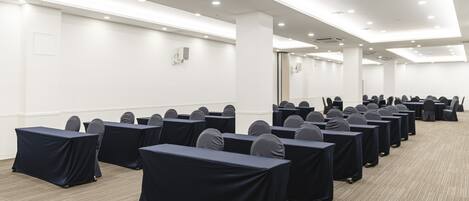 A conference room with rows of tables and chairs, white walls, and a carpeted floor.