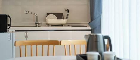 A modern kitchen with white cabinets, a stainless steel sink, and a dish rack. There is a coffee maker and a kettle on the counter.