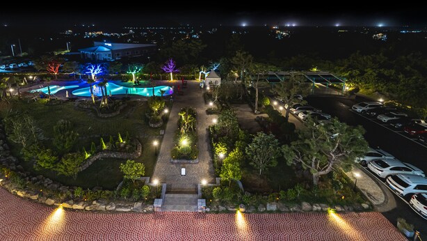 A landscaped area with a swimming pool, pathways, and a parking lot at night. - Hallim Resort (Jeju City)