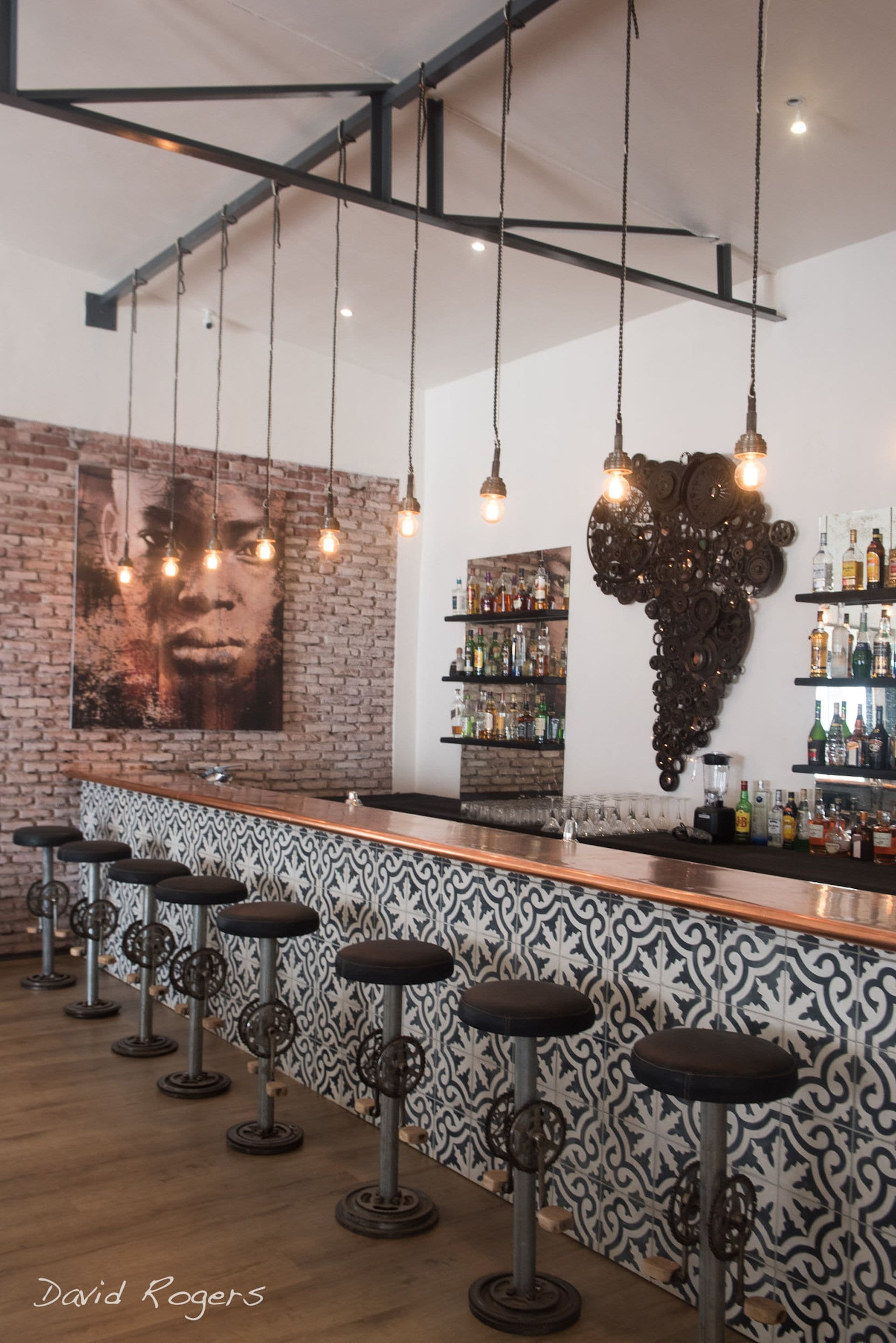 A bar area with a brick wall, hanging lights, a large decorative headpiece, and a patterned backsplash.