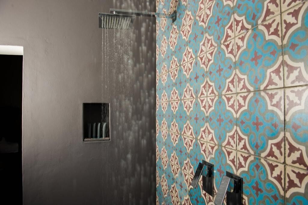 A bathroom with a shower, a small window, and a tiled wall with a geometric pattern.