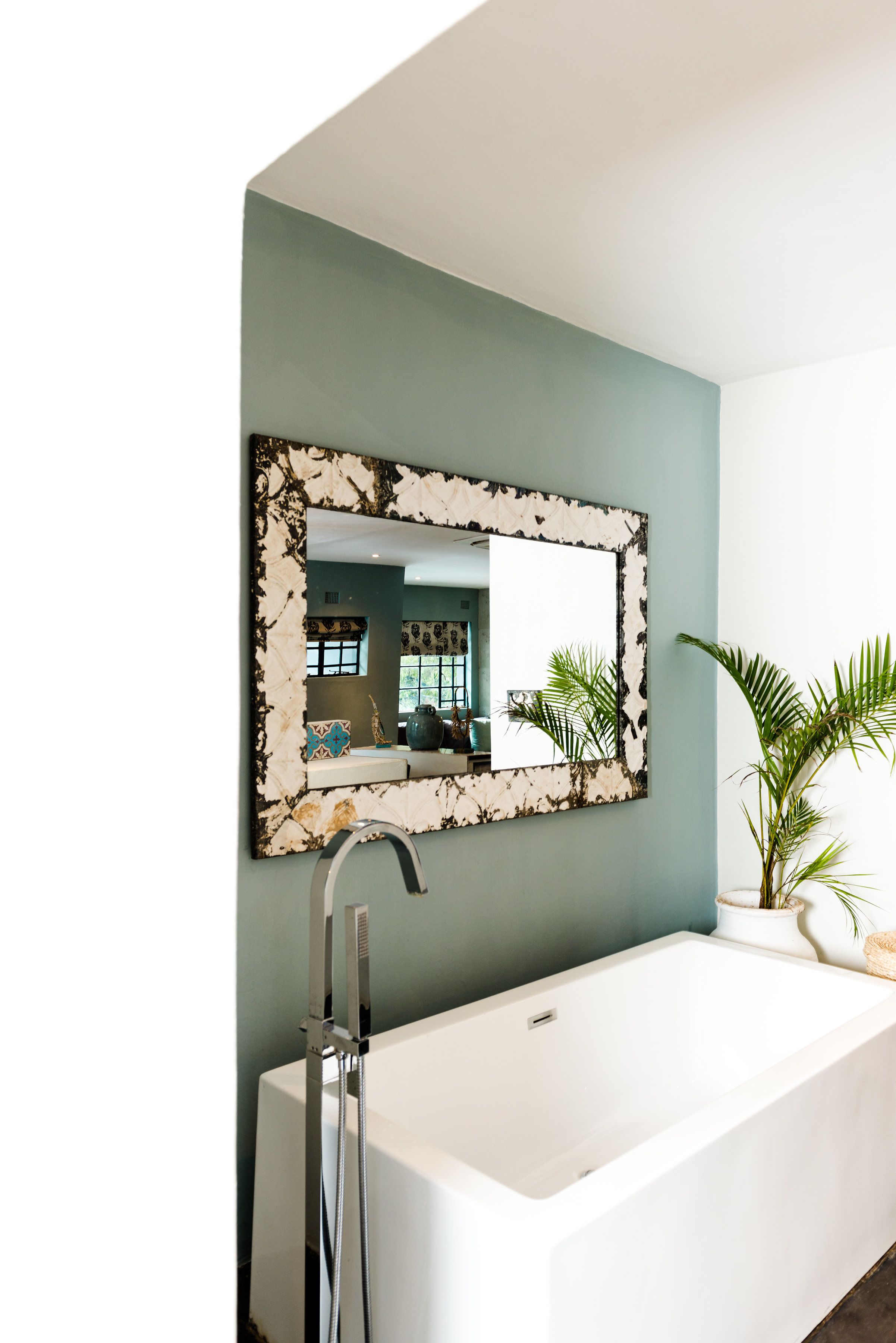 Un baño moderno con una bañera blanca, un espejo grande con marco decorativo y una planta en maceta.