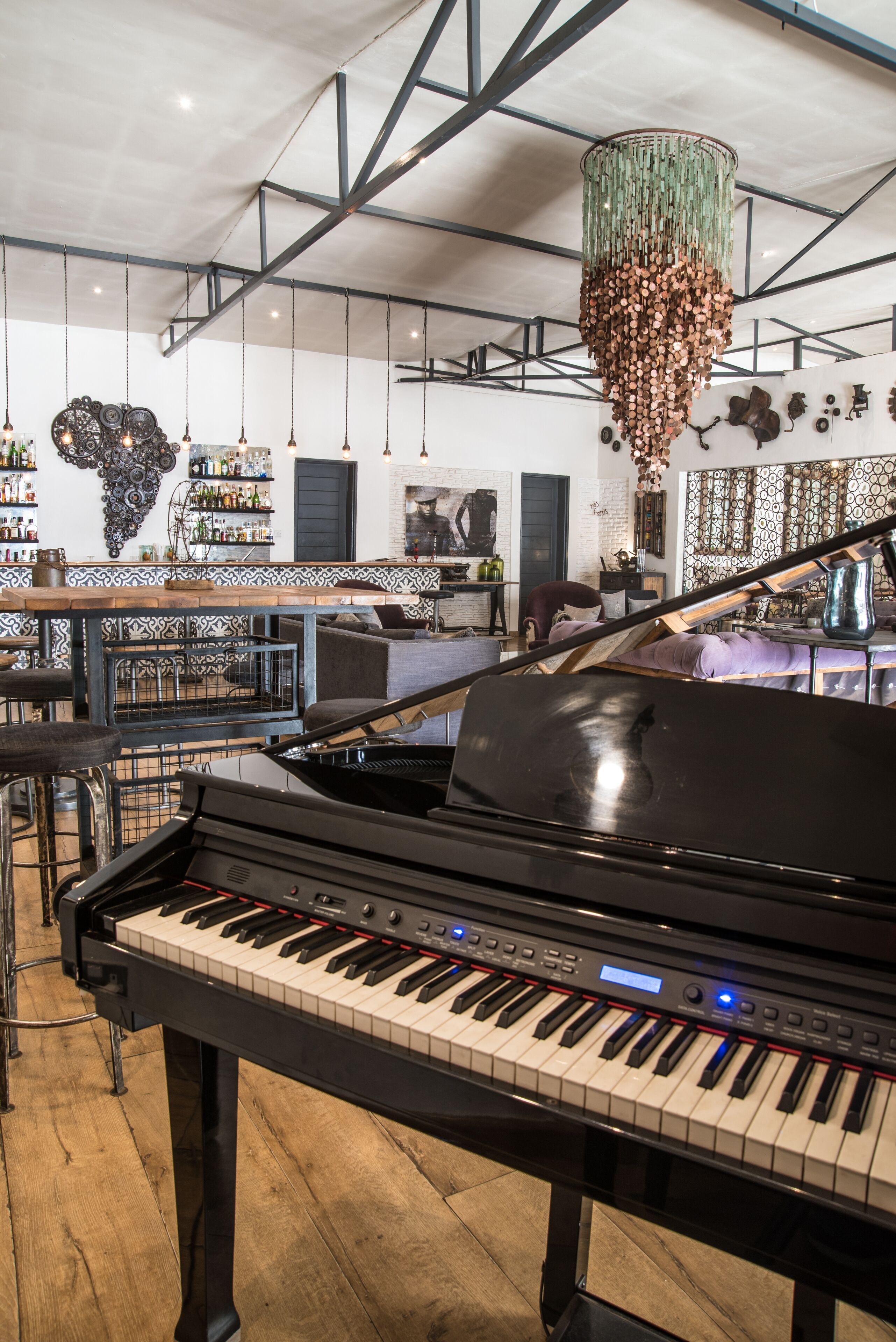 Un piano en una habitación amplia con techo alto, una zona de bar con estantes llenos de botellas y una lámpara original.