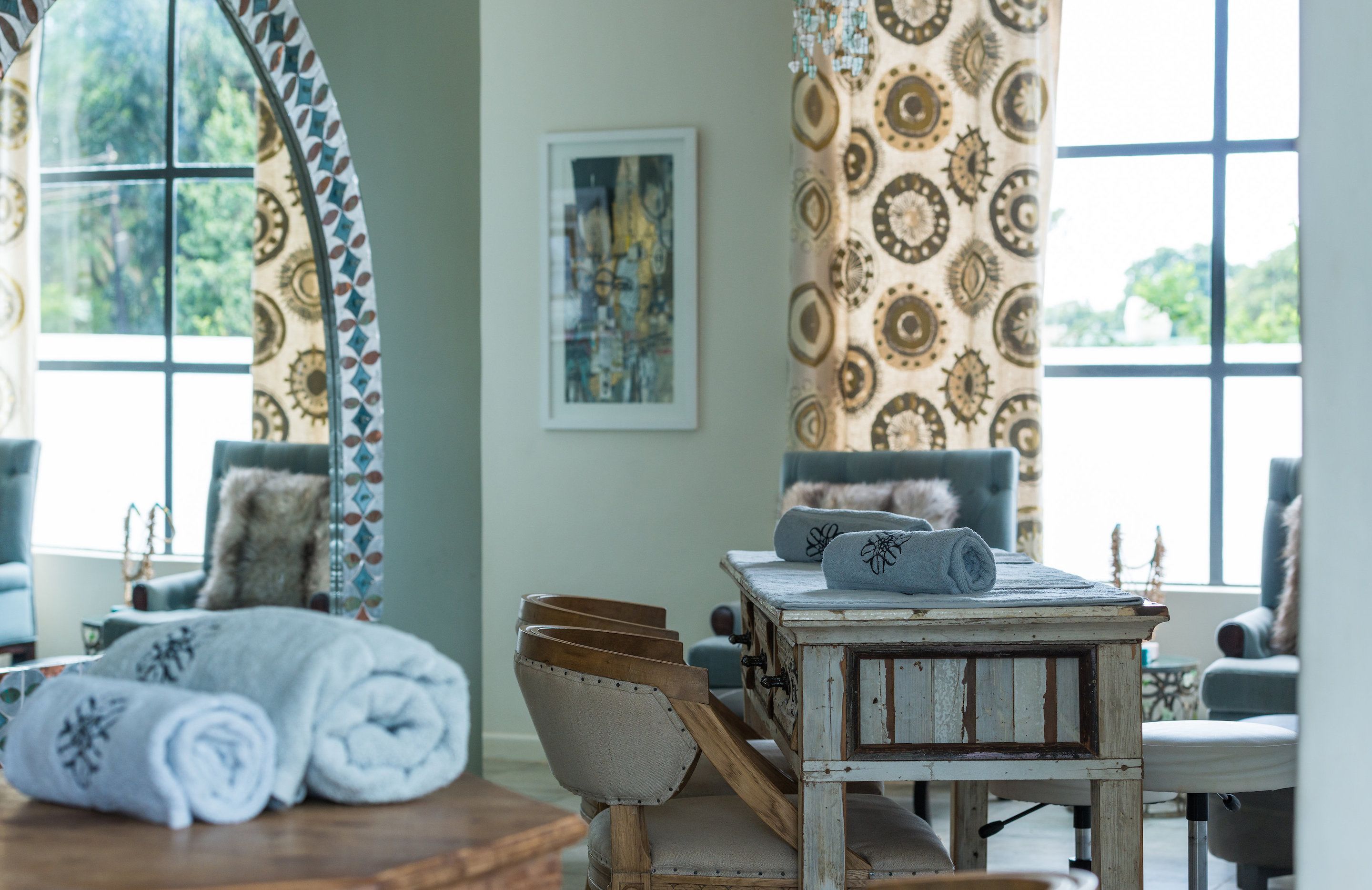 A cozy room with a wooden table, a chair, and a sofa. There are towels on the table and a framed picture on the wall.