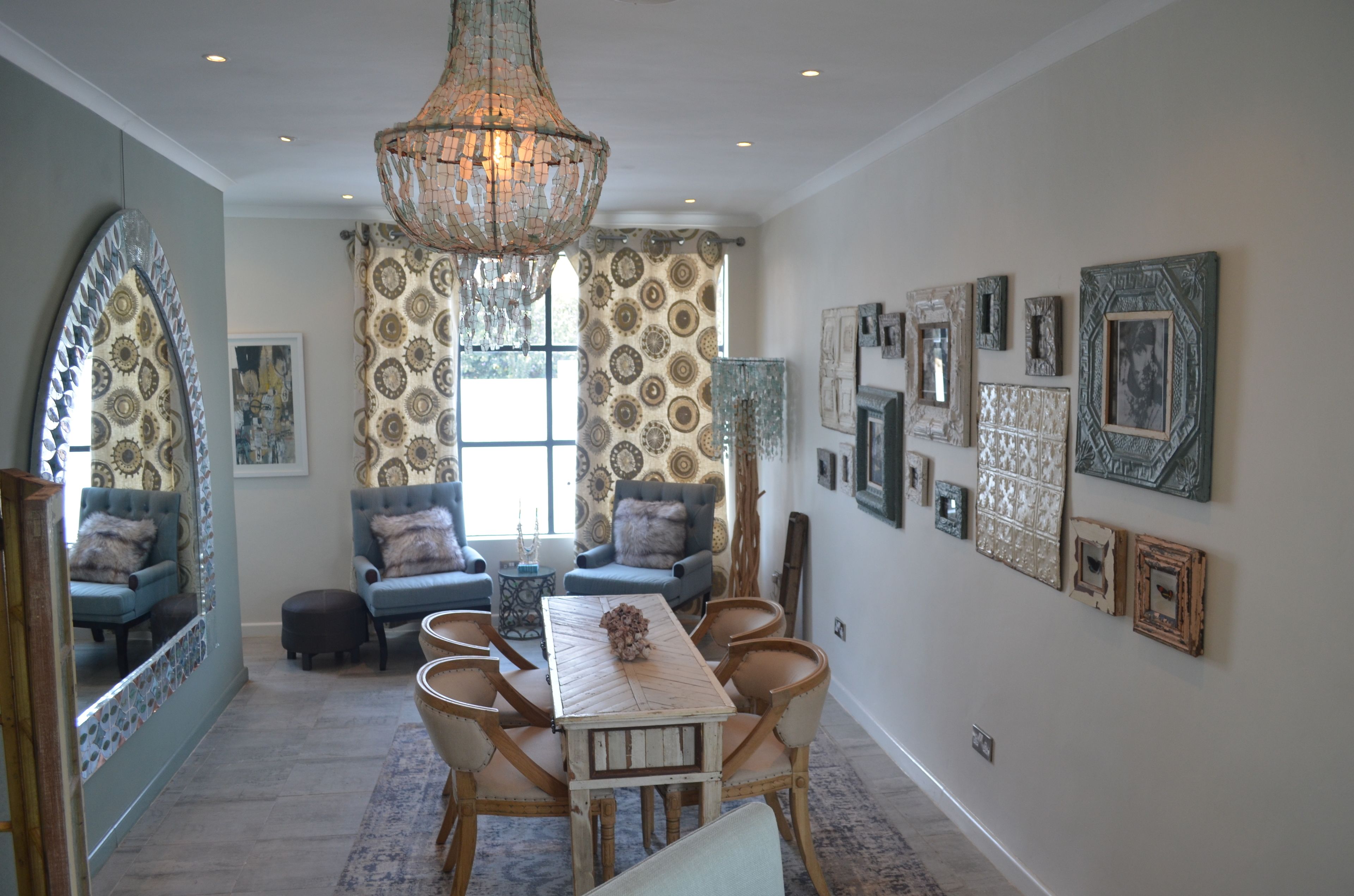 A dining area with a wooden table and chairs, a chandelier, patterned curtains, and wall-mounted artwork.