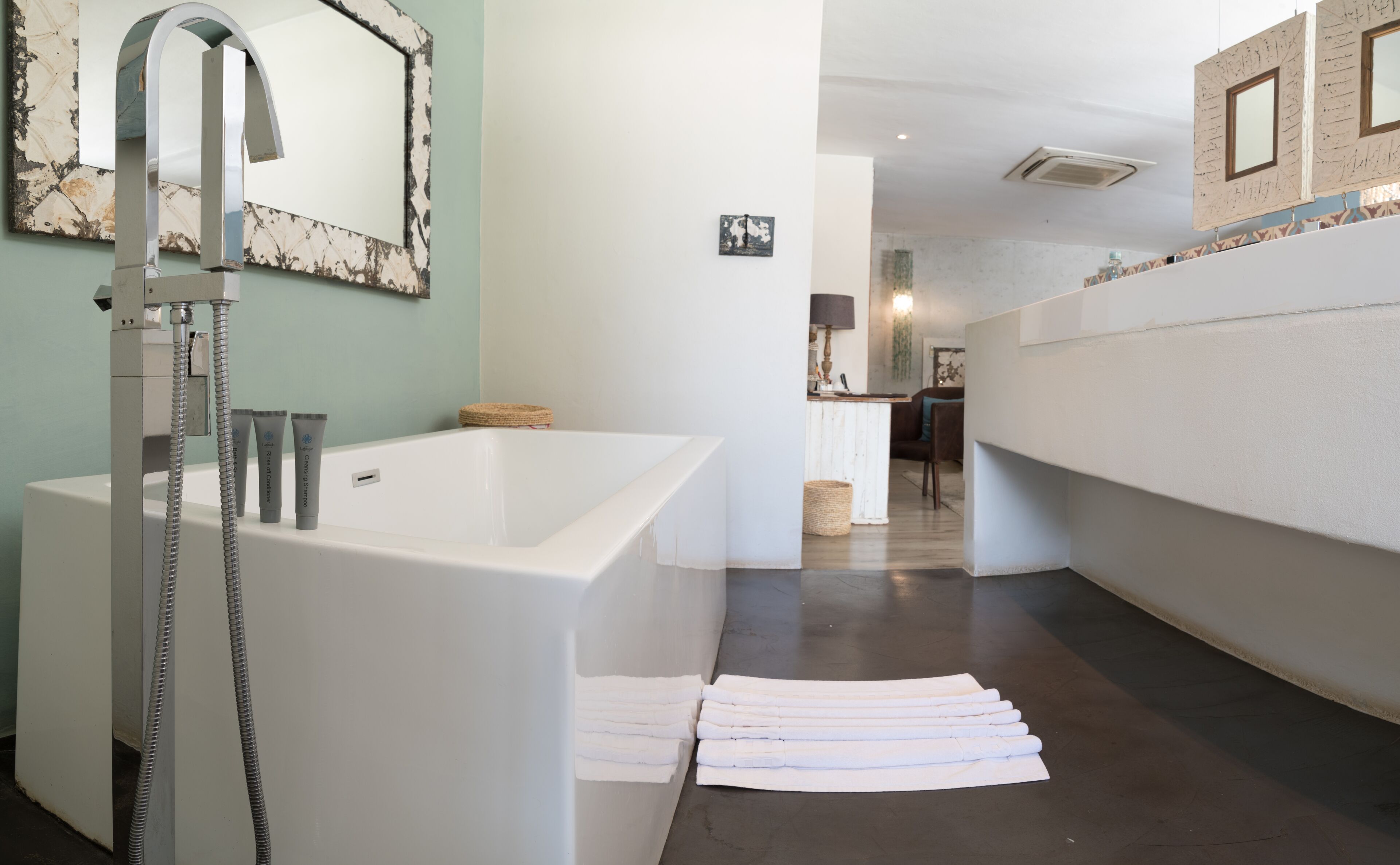 Ein modernes Badezimmer mit einer großen Badewanne, einer Dusche mit einem hohen Wasserhahn und einem Waschbeckenbereich.