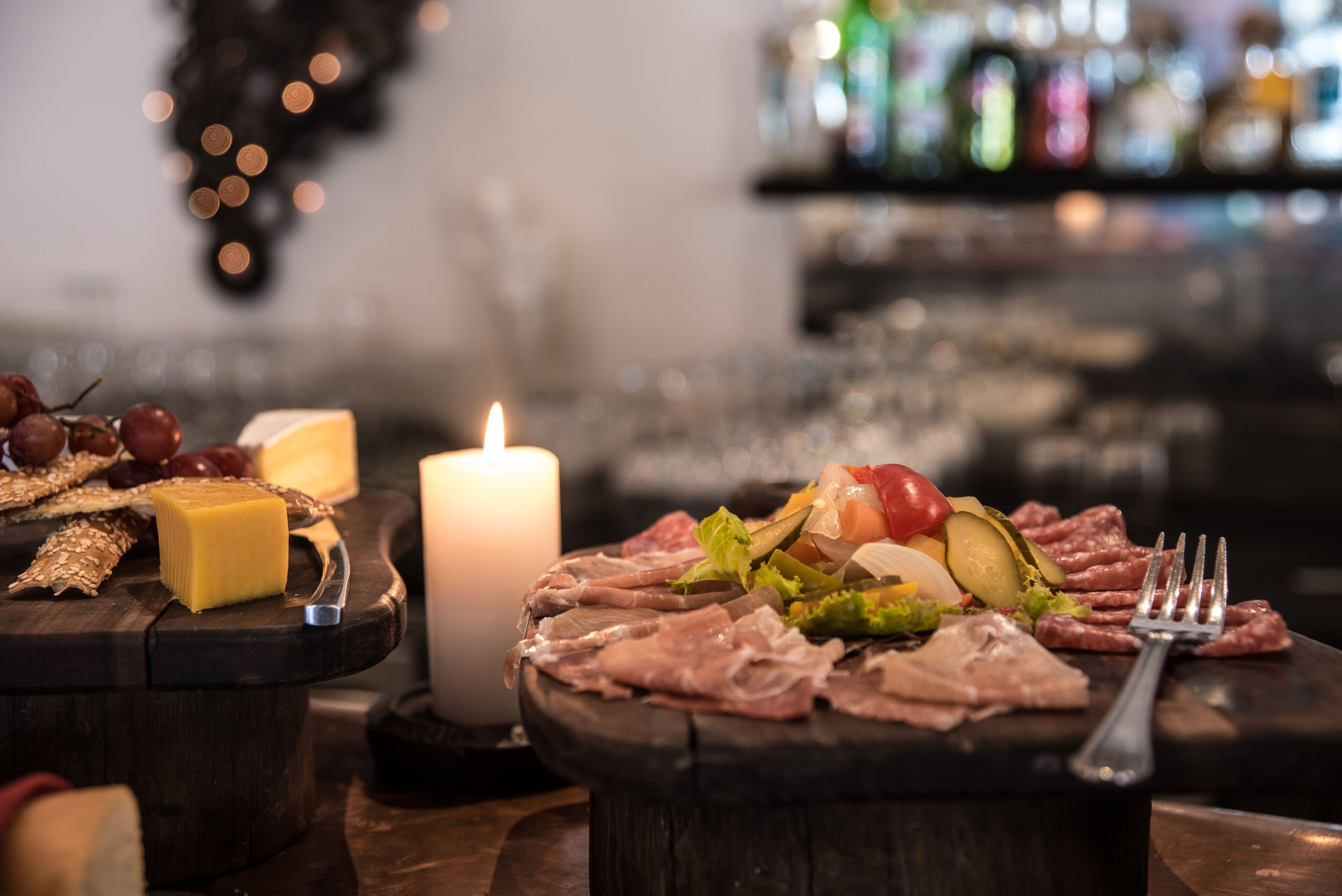 Ein Tisch mit verschiedenen Käsesorten, Wurstwaren und einer brennenden Kerze, was auf eine Esssituation hindeutet.