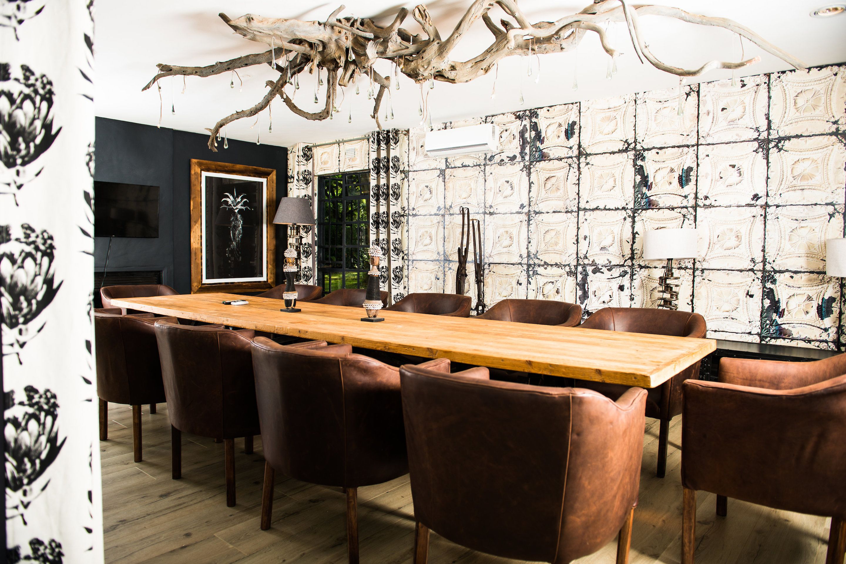 A dining area with a long wooden table and brown leather chairs, surrounded by patterned wallpaper and a large decorative branch overhead.